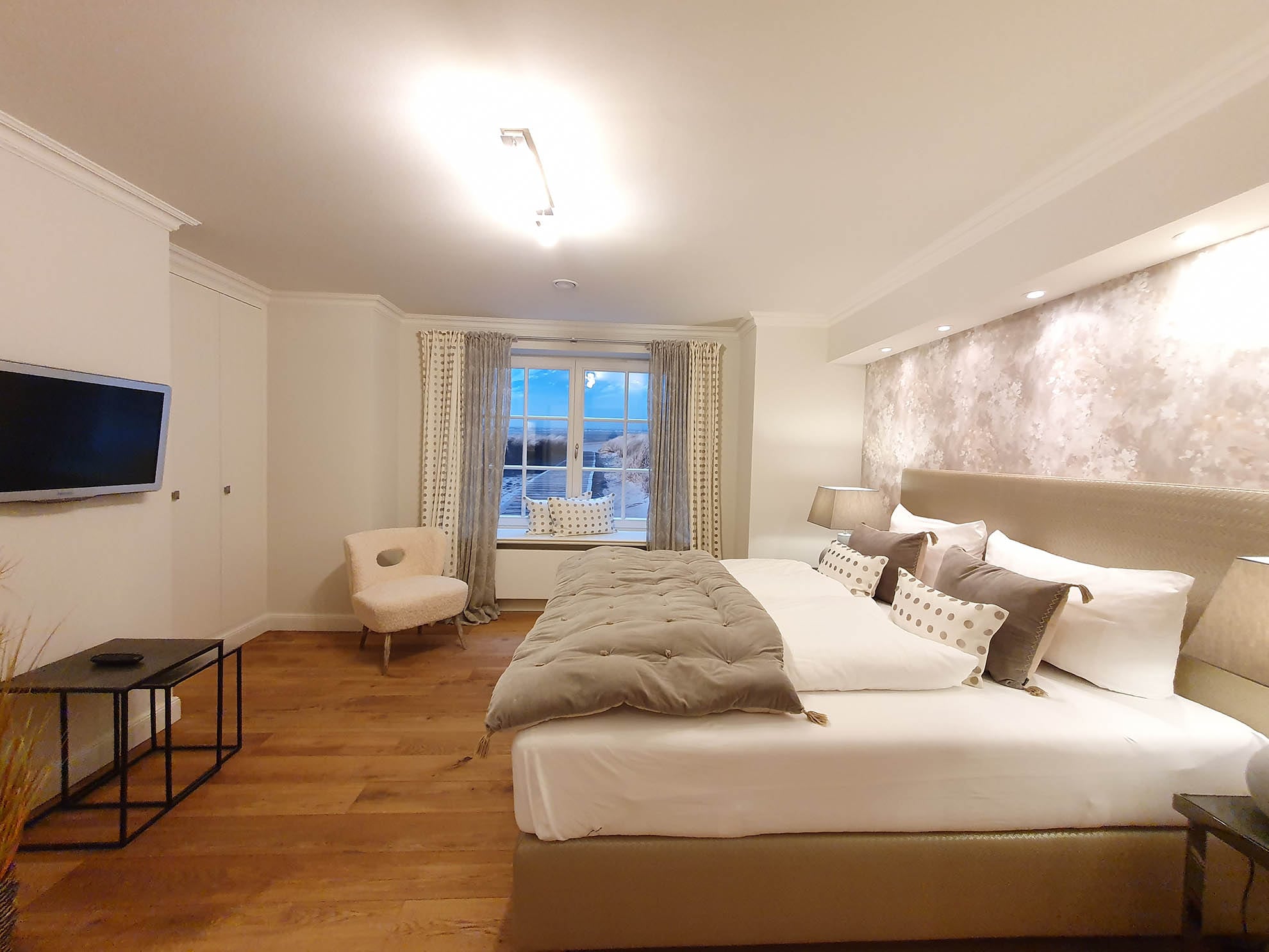 Schlafzimmer mit großen Fenstern und Fernseher Alter Post II Hotel Duene Sylt